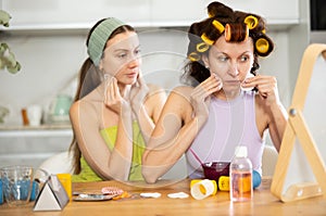 Female friends removing cosmetics with cotton rounds by mirror