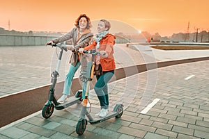 Female friends ride modern rented electric scooters through the streets of the city. Transport and lifestyle and friendships