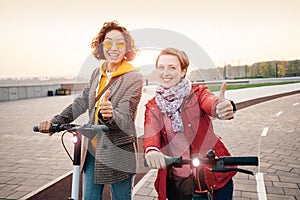 Female friends ride modern rented electric scooters through the streets of the city. Transport and lifestyle and friendships