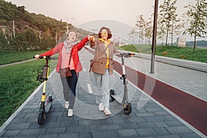 Female friends ride modern rented electric scooters through the streets of the city. Transport and lifestyle and friendships