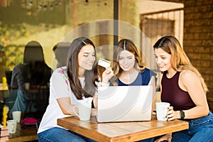 Female friends shopping online at cafe