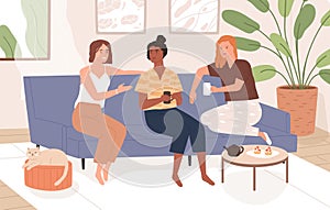 Female friends sitting on comfy sofa, talking and drinking tea. Happy smiling women chatting and relaxing on couch