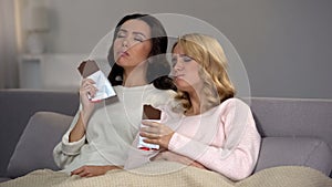 Female friends sitting on sofa and enjoying sweet chocolate taste, hormones