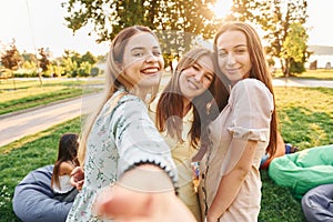 Female friends standing and having fun. Group of young people have a party in the park at summer daytime