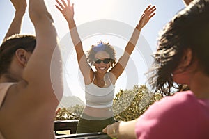 Female Friends Standing Up Through Sun Roof Car And Dancing On Road Trip Through Countryside
