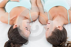 Female friends in teal tank tops lying in bed