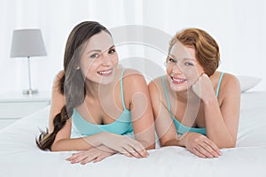 Female friends in teal tank tops lying in bed