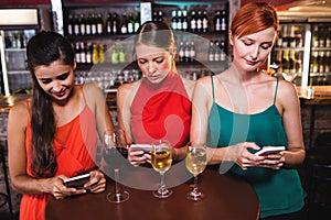 Female friends using mobile phone while enjoying wine