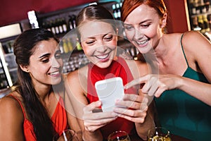 Female friends using mobile phone while enjoying wine