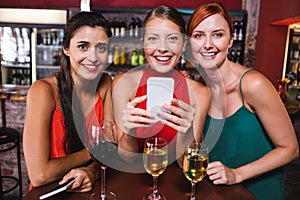 Female friends using mobile phone while enjoying wine