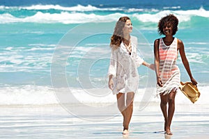 Female friends walking barefoot by the water on a beach