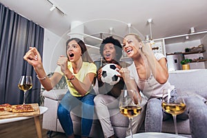 Female friends watching soccer match and celebrating victory at home