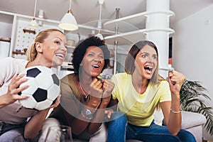 Female friends watching soccer match and celebrating victory at home