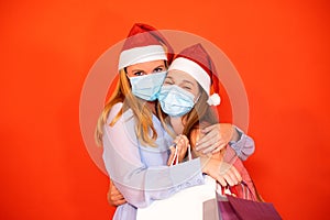 Female friends wearing surgical mask and Christmas hat holding shopping bags on a vivid red orange background