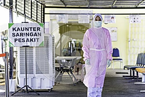 Female frontliner in Malaysia performing her tasks during the coronavirus pandemic while wearing full PPE standing beside a signbo