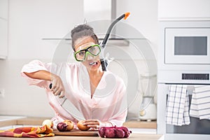 Female with a funny face expression protects herself from onion cutting smell by a snorchel while standing in the kitchen dressed