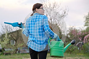 Female gardener holding watering can and garden tools