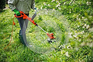 Female gardener using electric string trimmer to trim grass in garden