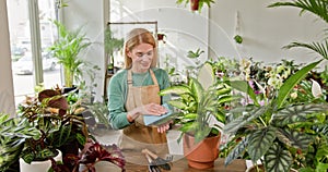 A female gardener, working in a sunlit flower shop, cares for various indoor plants, showcasing a passion for greenery