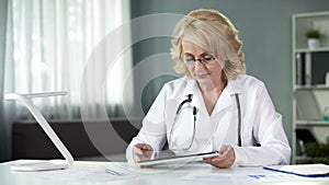 Female general practitioner reading patient's online medical records on tablet