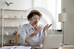 Female general practitioner wears headset video conferencing on laptop photo