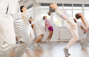 Female girl student repeats movements of unrecognizable teacher during group modern dance class.