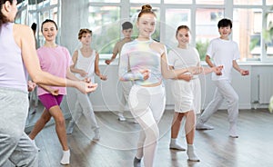 Female girl student repeats movements of unrecognizable teacher during group modern dance class.
