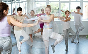 Female girl student repeats movements of unrecognizable teacher during group modern dance class.