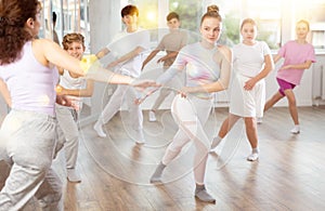 Female girl student repeats movements of unrecognizable teacher during group modern dance class.