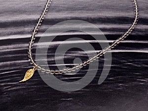 Female golden wing shaped pendant with transparent beads chain necklace on black rippled background