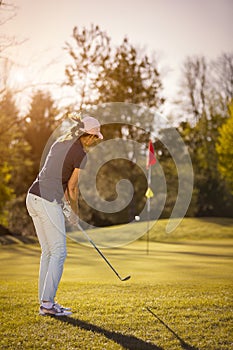 Female golf player pitching towards flag.