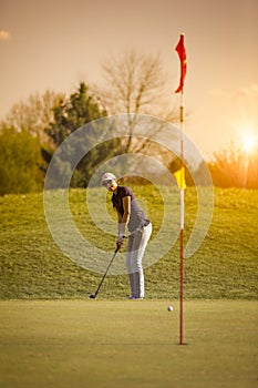 Female golf player putting at sunset.