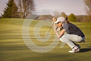 Female golf player squatting on green.