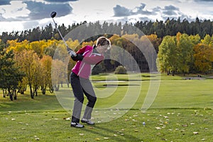 A female golf player swinging driver, long driving, on an autumn day, at the golf course.