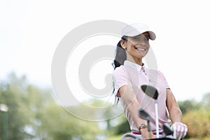 Female golfer smiles and holds bag of golf clubs