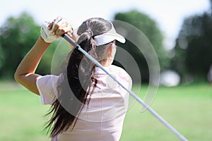 Female golfer stands with her back and holds golf club in her hands.