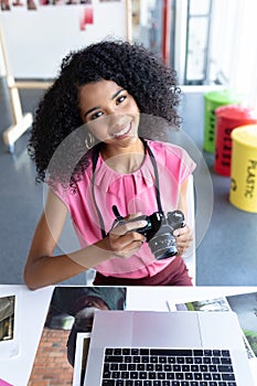 Female graphic designer reviewing photos on digital camera at desk in office