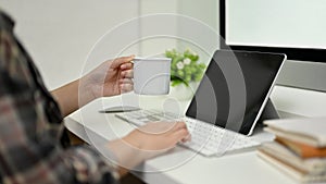 A female graphic designer sipping coffee while working at her desk, typing on keyboard