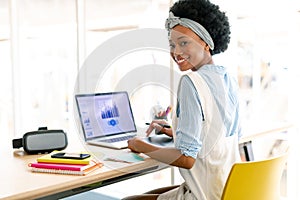 Female graphic designer using graphic tablet while looking at laptop at desk