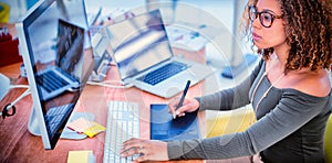 Female graphic designer working on computer while using graphic tablet at desk