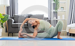 Female in green top and leggings stretching in Parivrtta Janusirsasana exercise or Revolved Head to Knee Pose on blue mat in