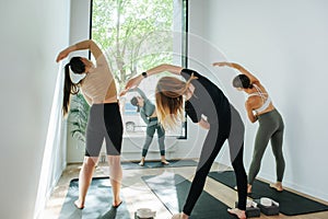 Female group practicing yoga in front of an instructor, doing side bends