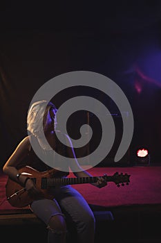 Female guitarist playing guitar while sitting on stage