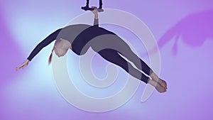 Female gymnast isolated on pink background. Girl aerial dancer balancing flying on trapeze with straps up in the air