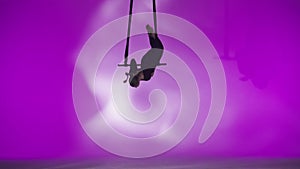 Female gymnast isolated on pink neon studio background. Girl aerial dancer balancing spinning on gymnastic trapeze with