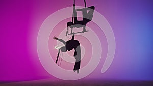 Female gymnastic duet isolated on laser blue neon studio background. Girls aerial dancers flying on gymnastic trapeze