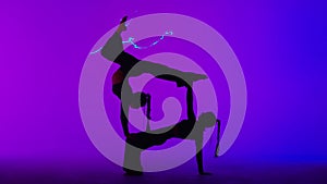 Female gymnastic duet isolated on laser blue neon studio background. Girls dancers showing gymnastic elements on the