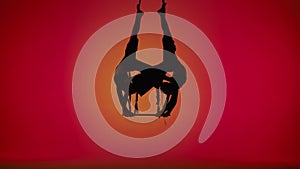 Female gymnastic duet isolated on orange neon studio background. Girls aerial dancers flying on acrobatic trapeze with