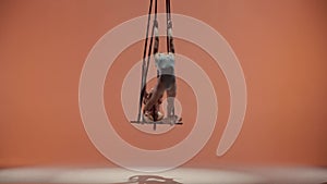 Female gymnastic duet isolated on peach studio background. Girls aerial dancers flying and hanging high on trapeze with