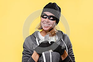 A female hacker in a black hat and a mask-glasses, greedily holds a wad of money in her hands and smiles. Yellow